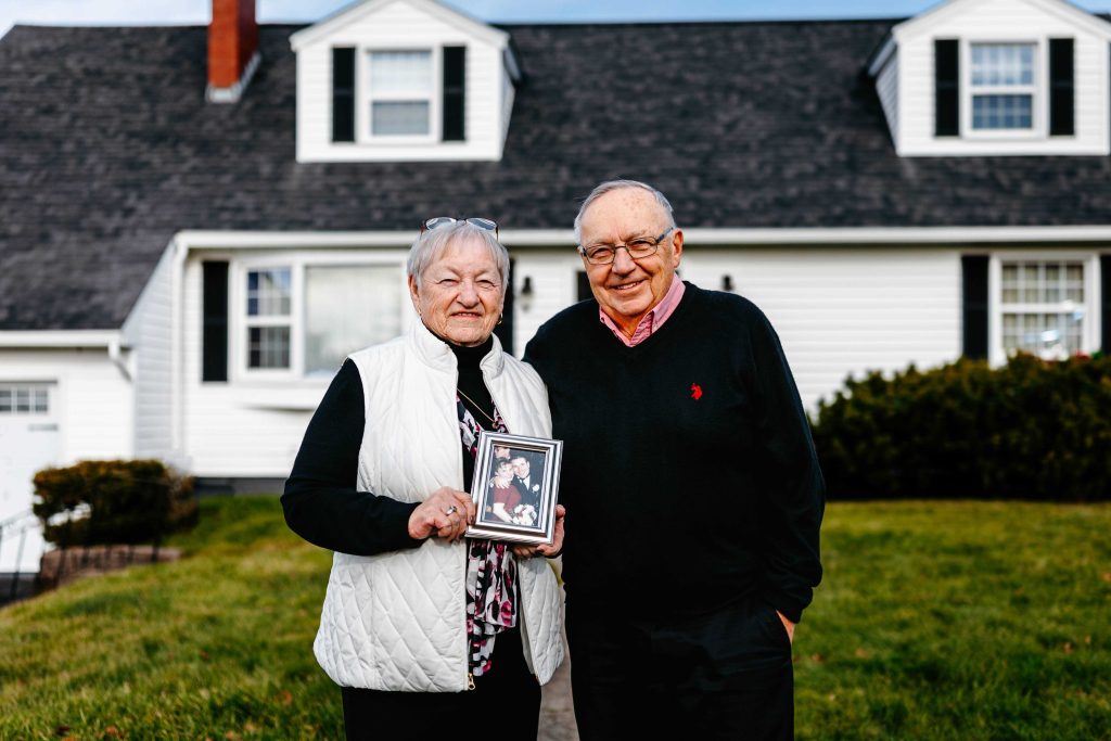 Jack and Mary-Lee McMillan stand at their family home with a photo of John and Cheri.